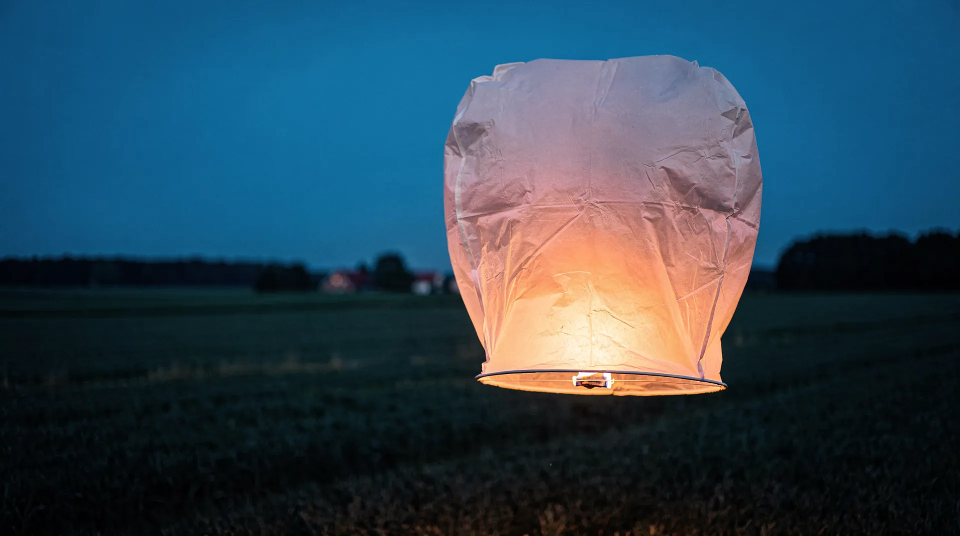 LED-Himmelslaterne ohne Feuer aufsteigend in den Abendhimmel über einem ruhigen See